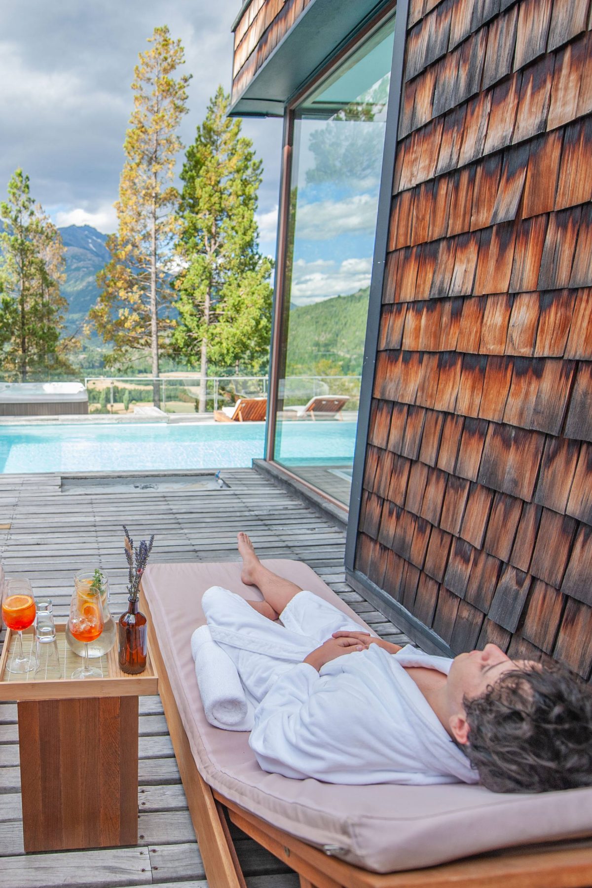Huésped descansando en bata junto a la piscina exterior, con tragos servidos en la mesa lateral