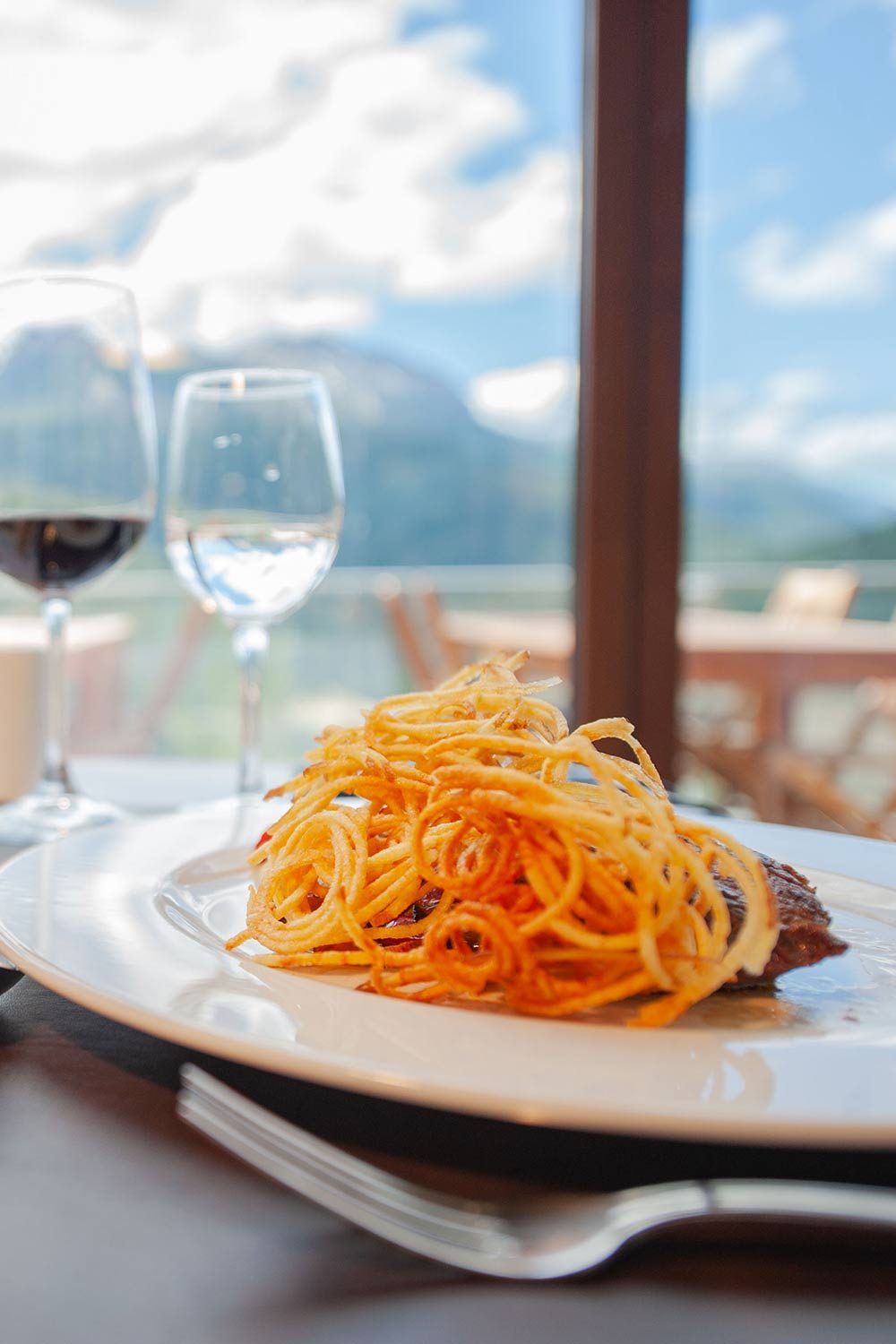 Plato servido junto al ventanal con vista a la cordillera y copas de vino